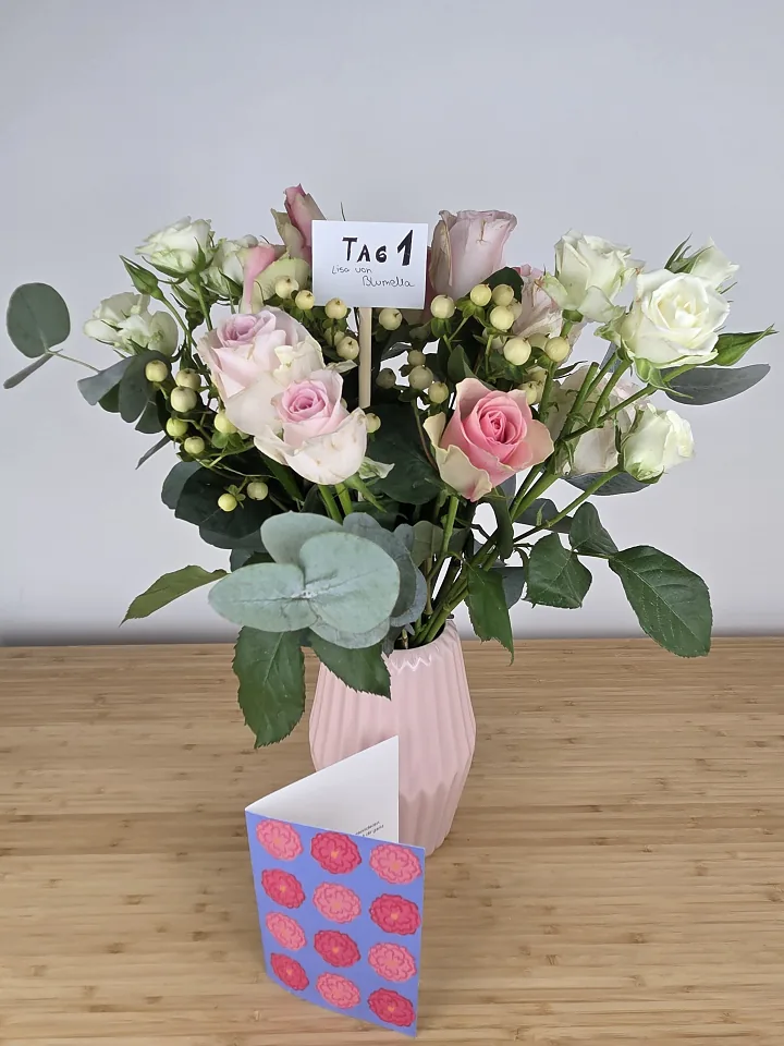Bloom & Wild Fairtrade-Strauß Rosengarten am Liefertag mit zartrosa Rosen, Hypericum-Beeren und Eukalyptus, davor die Grußkarte mit Pfingstrosen