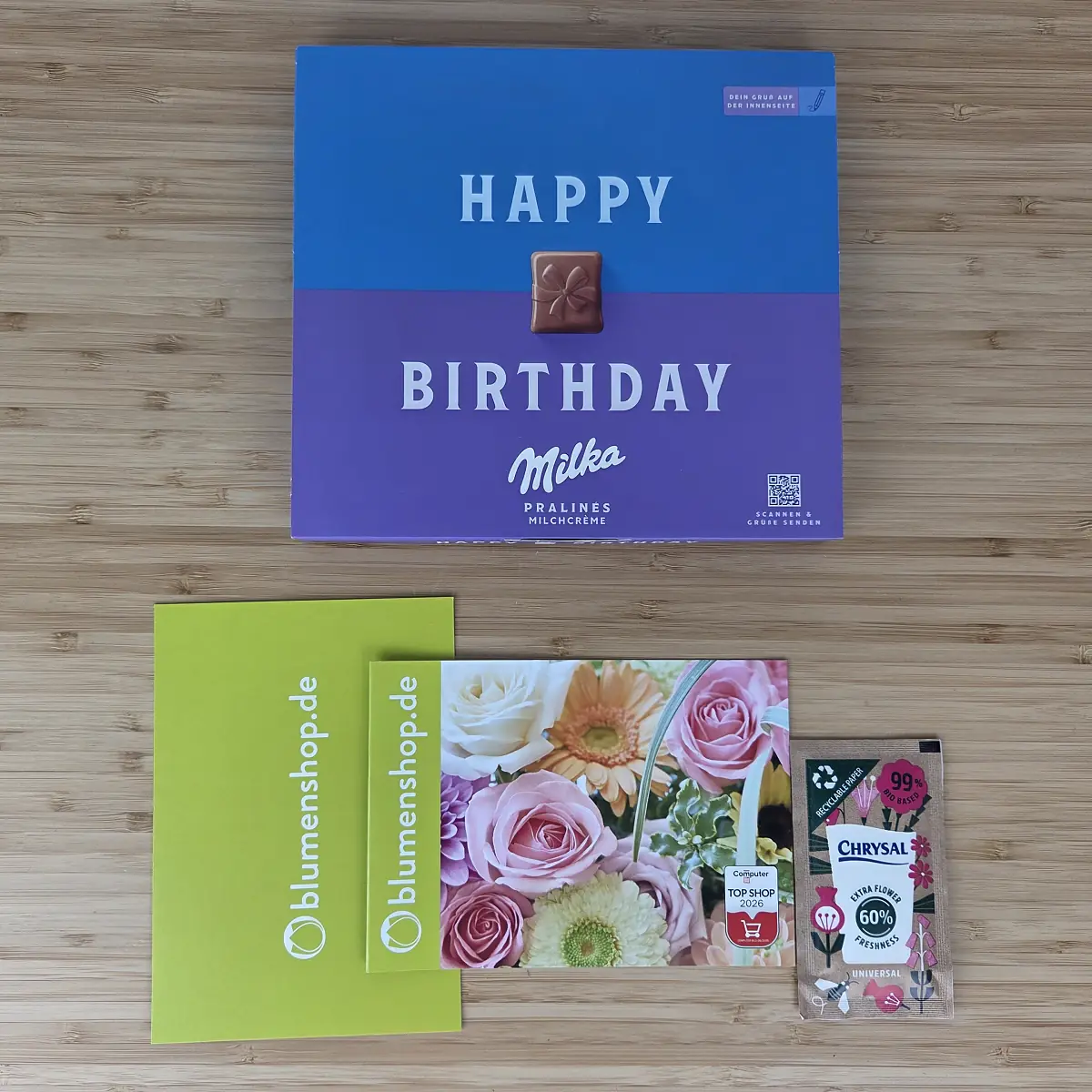 Beigaben der blumenshop.de Ersatzlieferung: Milka Happy Birthday Pralinen, grüne Grußkarte, Pflegeanleitung und ein Tütchen Blumennahrung
