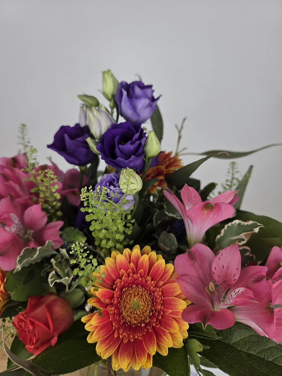 Nahaufnahme eines Bluvesa-Straußes mit lila Lisianthus, orangefarbener Gerbera, pinken Alstromerien und hellgrünem Thlaspi