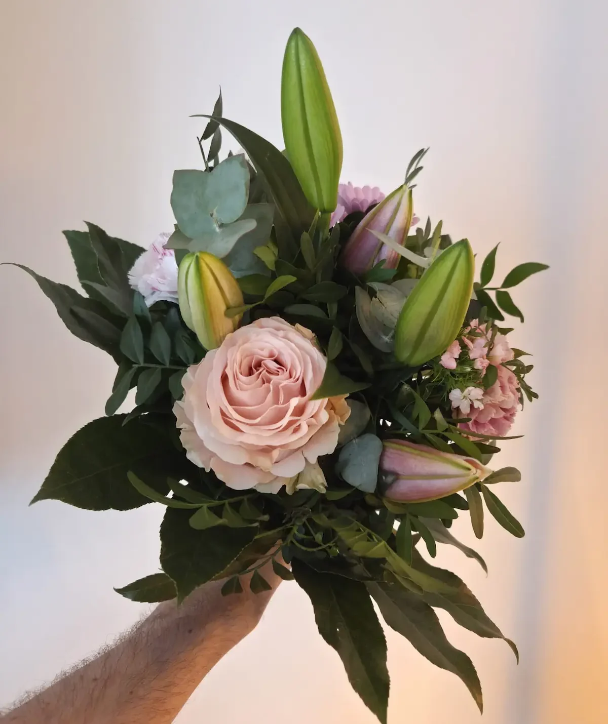 Unser Euroflorist-Teststrauß am Liefertag, in der Hand gehalten: zartrosa Rose, Lilienknospen, Nelken und Eukalyptus