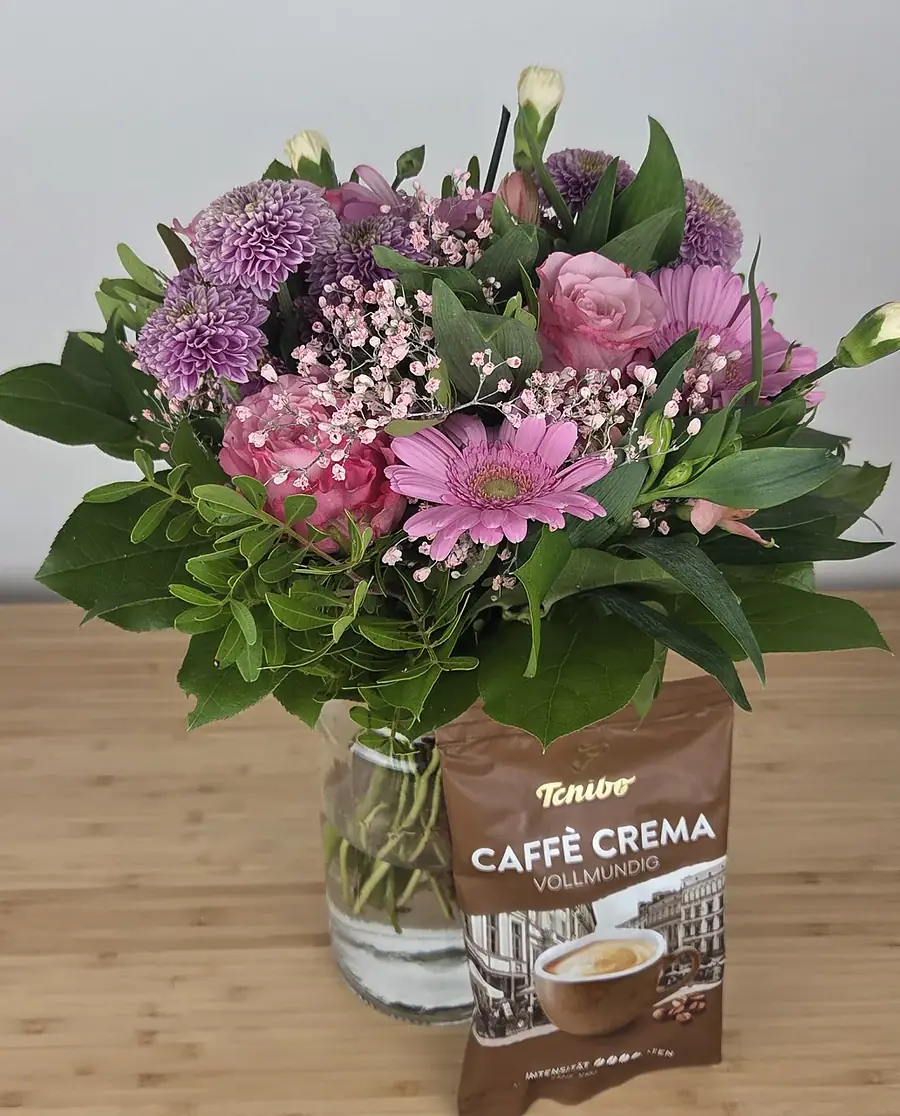 BLUME2000 Strauß Schön dass es dich gibt aus unserem Testkauf, rosa und lila Chrysanthemen, Rosen und Gerbera, daneben die gratis Tchibo-Kaffeepackung