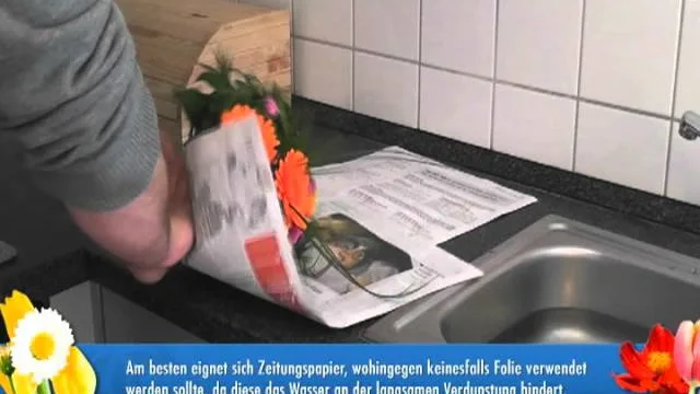 Ein in Zeitungspapier gewickelter Strauß steht zum Aufpäppeln in einem Glas Wasser